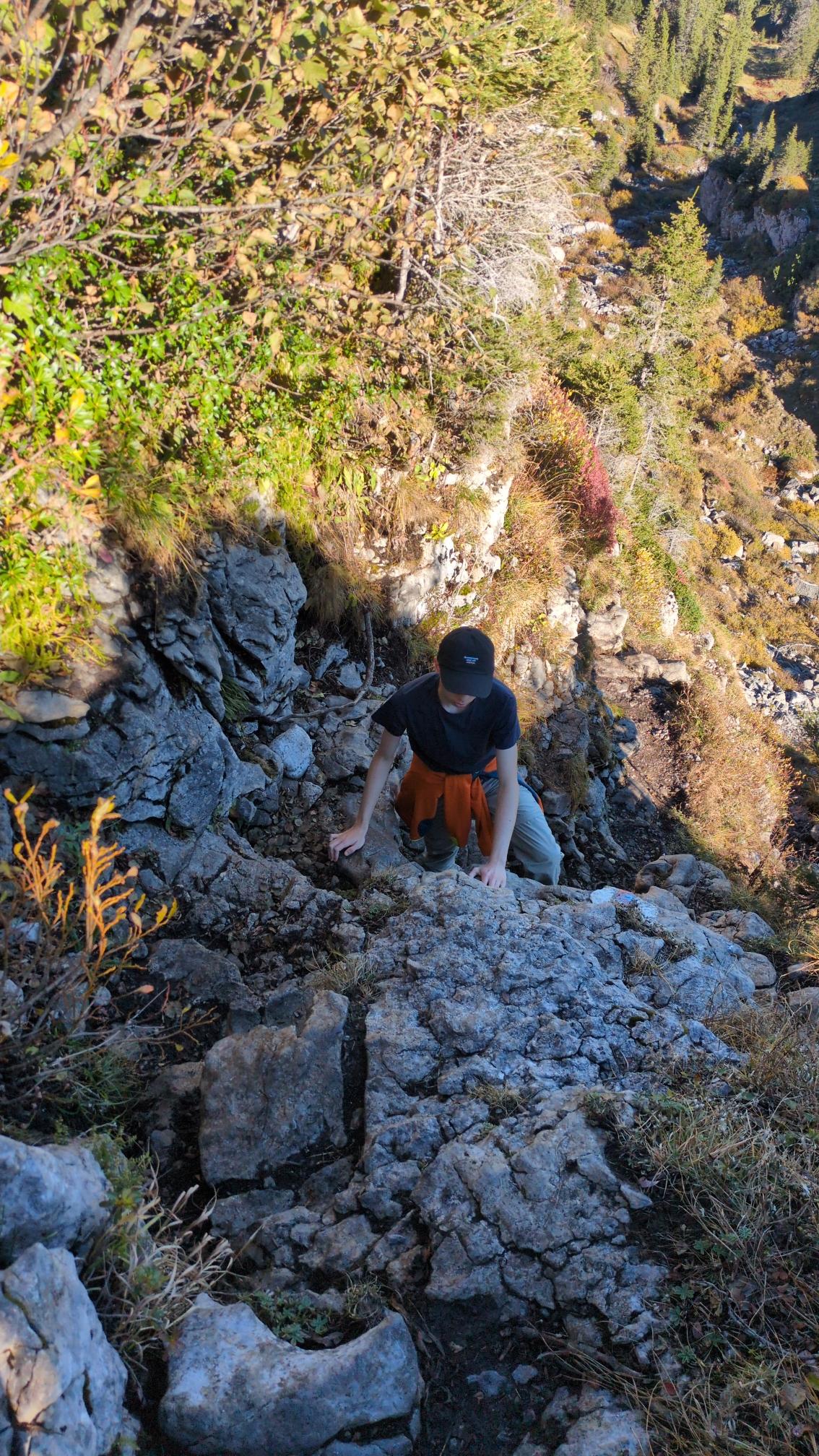 My son with a black cap climbing up the first steep part of the ascent.
grey limestone, bushes and below us some trees.