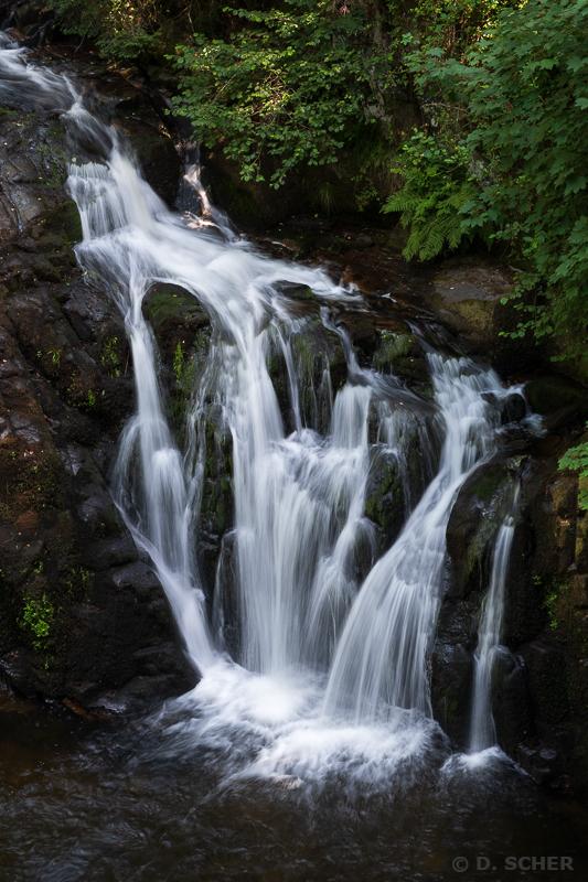 The water flow splits into multiple small waterfalls when it encounters several moss-covered rocks. The long exposure gives a silky look to the water.
