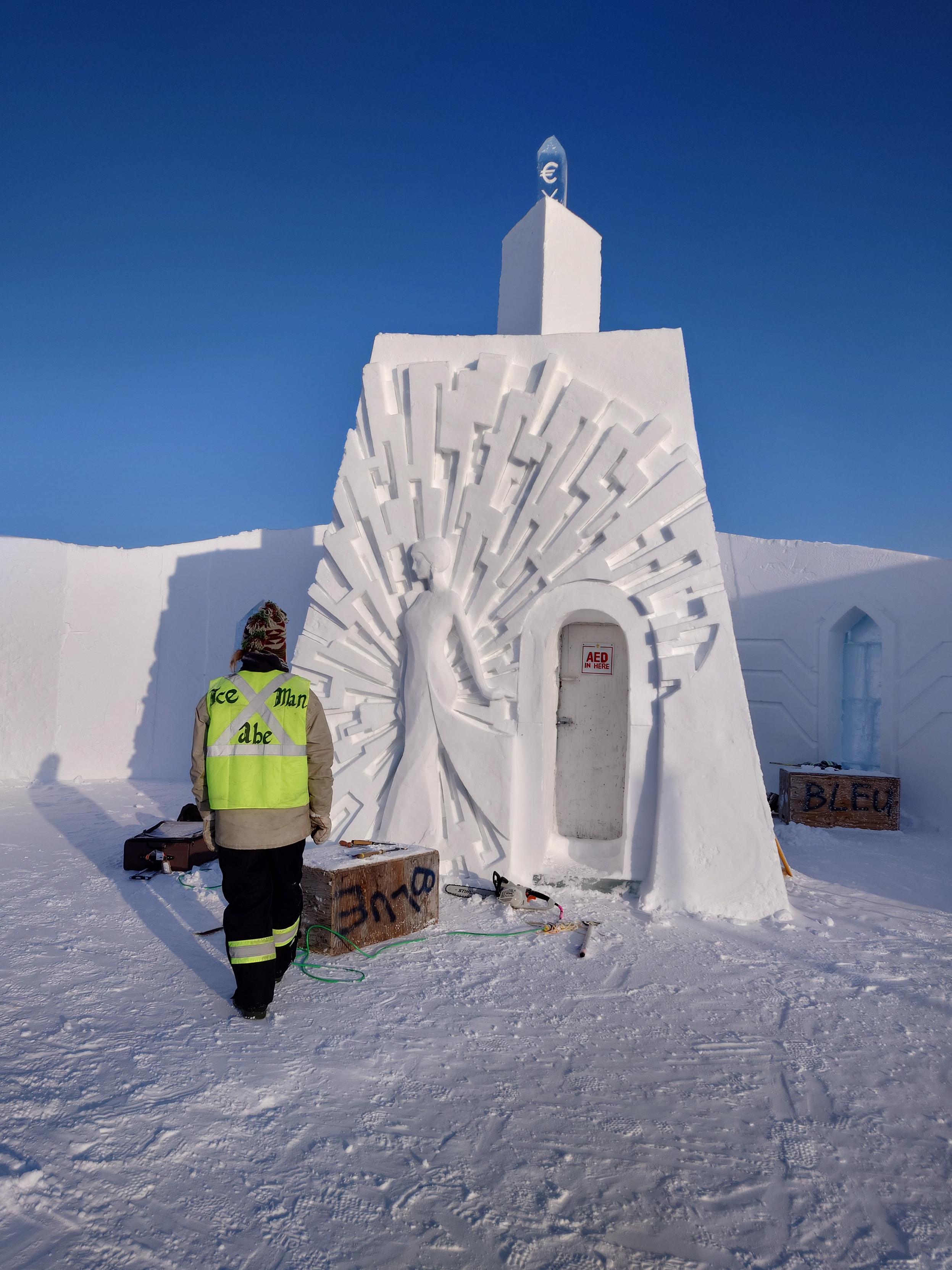 A carver in a reflective vest considers the snow wall he has been working on.