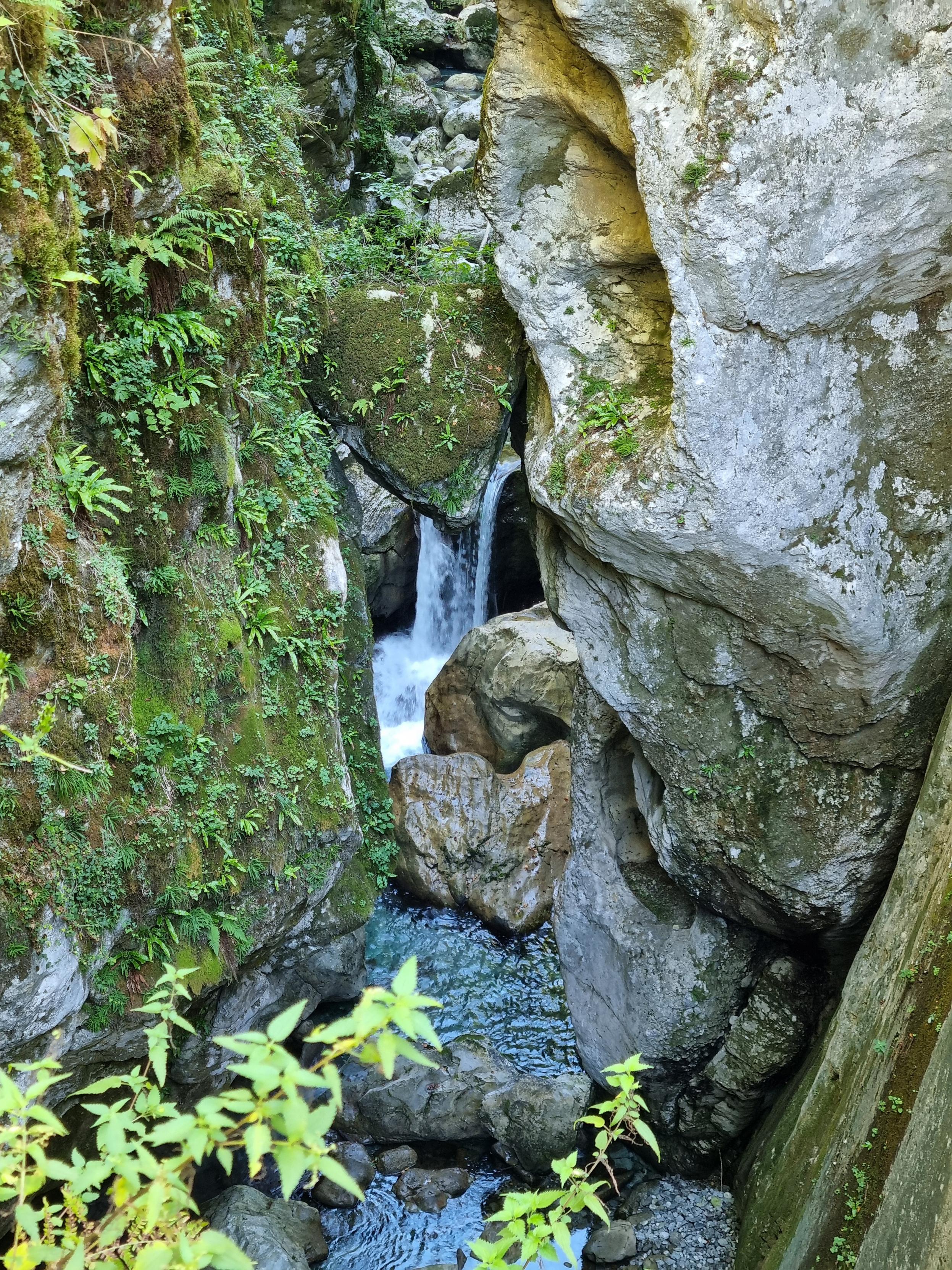 Stone trapped in between the side walls of a gorge. Waterfall in the background